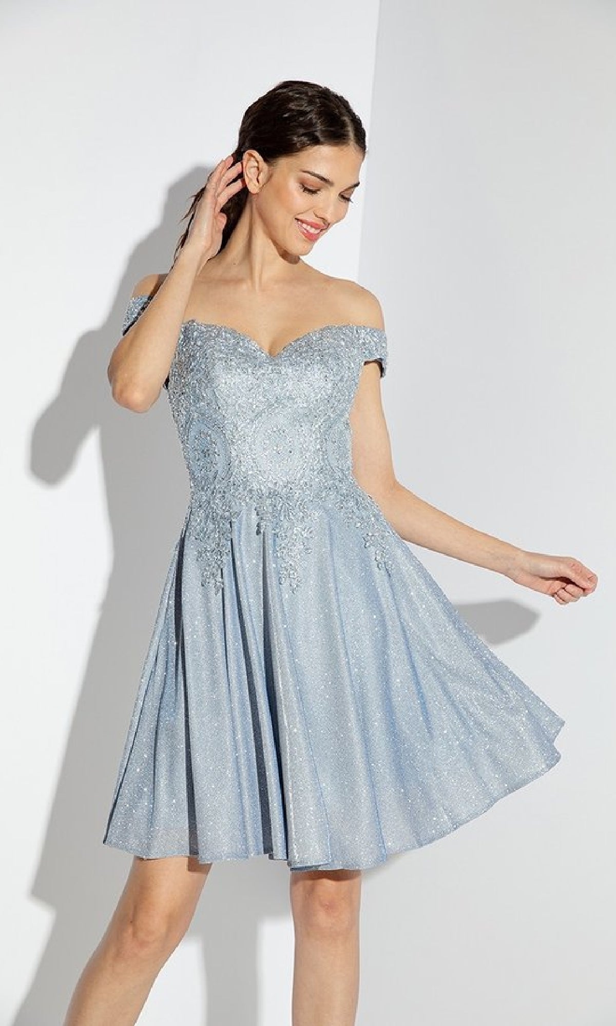 A woman poses against a white background wearing the Off-Shoulder Short Glitter Hoco Dress: Eureka 9366, a light blue sparkly cocktail dress with an off-the-shoulder design.